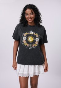 Black cotton t-shirt with a colorful sun and floral graphic design. Loose fit, short sleeves, paired with a white eyelet trim skirt.
