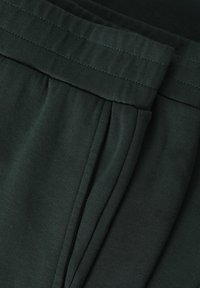 Dunkelgrüder Stoff mit weicher Textur, ausgestattet mit einem gefalteten Bund und Falten, die einfache Nähedetails zeigen.