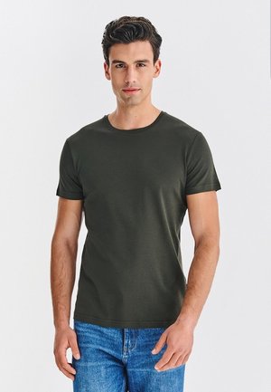 Ciemnozielona koszulka z krótkim rękawem, wykonana z gładkiego materiału z okrągłym dekoltem, zestawiona z jasnoniebieskimi dżinsami.