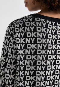 Svart strikkegenser med et gjentatt hvitt "DKNY" logo-mønster, rund hals og teksturert stoff. Ideell for hverdagsbruk.