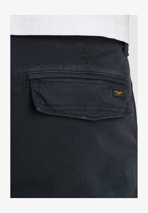 Sorte stofbukser med en baglomme, der har en klap, syet detalje og et lille guldlogo på lommen. Glat tekstur.