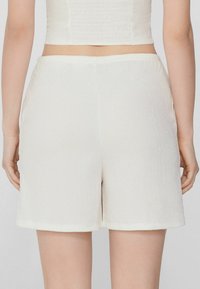 Shorts bianchi con texture e vestibilità comoda. Il materiale presenta un leggero motivo stropicciato e un'orlo pulito. Visibile la fascia elastica in vita.