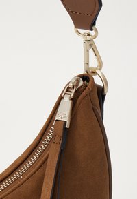 Pruun suede kott kuldse tooni riistvara, millel on lukuga sulgur ja klamber. Elegantne kõver kuju sujuva tekstuuriga.