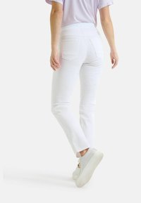 Weiße Jeans mit geradem Bein, ausgestattet mit Gesäßtaschen und einer glatten Textur. Kombiniert mit weißen Sneakers.