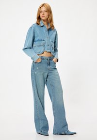 Ljusblå denimjacka med kort längd och två framlösa fickor, tillsammans med högmidjade vida jeans med slitet utseende och rena fållar.