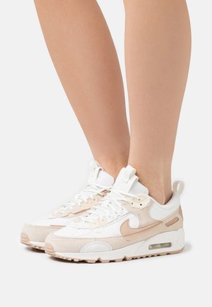 Chaussures de sport blanches et beiges en cuir suédé et en mesh, avec une semelle rembourrée et une unité d'air visible, des lacets et un marquage.