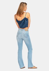 Niebieski bezrękawnik o marszczonym kroju zestawiony z jasnoniebieskimi dżinsami w fasonie dzwonów, które mają tylne kieszenie oraz brązową skórzaną naszywkę w pasie.