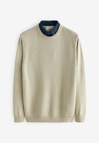 Pull en beige texturé avec un col rond, présentant une chemise à col bleu foncé contrastante en dessous, des manches longues et des poignets côtelés.