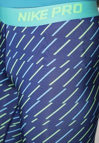 Leggings Nike Pro in blu navale con strisce diagonali in acqua e verde lime. Presentano una fascia in acqua solida con branding. Tessuto elasticizzato e testurizzato.