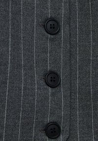 Gros plan de trois boutons noirs sur un tissu gris à fines rayures blanches verticales.