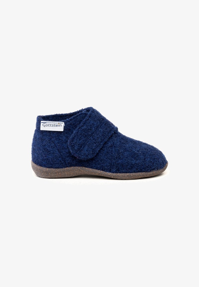 Navyblauer Wollschuh mit weicher Textur, niedrigen Schnitt und einem Klettverschluss für den Verschluss. Hat eine braune Sohle aus einem strukturierten Material.