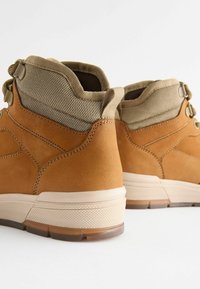 Brązowe zamszowe botki typu high-top z beżową siateczką na kostce i białą gumową podeszwą. Posiadają teksturowane przeszycia oraz podwójne zapięcia na sznurówki.