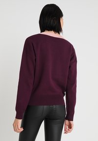 Fialový pletený svetr s růžovým akcentem na výstřihu, s volným střihem, spadlými rameny a žebrovaným lemem.