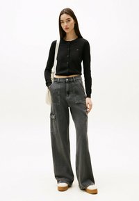Cárdigan negro recortado con botones en el frente, combinado con pantalones cargo grises de pierna ancha que cuentan con bolsillos y un corte relajado. Zapatillas blancas completan el conjunto.