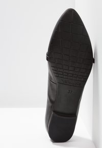 Semelle de chaussure noire à bout pointu avec motif de la bande de roulement, nom de la marque Tamaris, et taille 37 visible sur fond blanc.