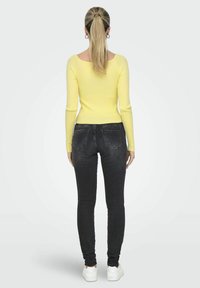 Geel geribbelde lange mouw top gecombineerd met donkere slim-fit jeans en witte sneakers, van achter bekeken. Eenvoudig en aansluitend ontwerp.