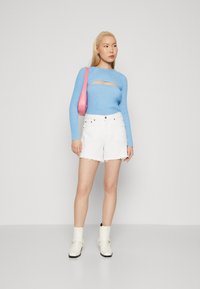 Top de manga larga de rayas azul claro con un corte; pantalones cortos de mezclilla blanca con dobladillo deshilachado; botines crema hasta el tobillo; bolso de hombro rosa.
