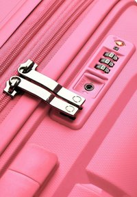 Pink hard-shell suitcase with a textured surface, dual silver zipper, and a combination lock display. Features a reinforced zipper track.