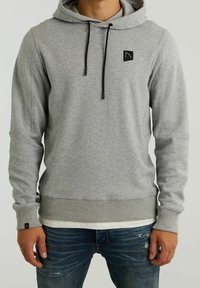 Sudadera gris hecha de un tejido suave, con un bolsillo frontal, cordones en la capucha y un pequeño parche con el logo en el pecho. Puños y dobladillo acanalados.