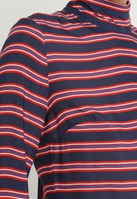 Maglione a collo alto a righe blu navy, con motivi orizzontali di righe rosse e blu chiaro. Tessuto morbido con un piccolo dettaglio tasca.