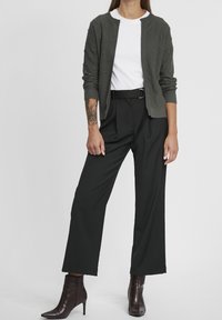 Texturowany ciemnozielony kardigan na białej koszulce, w połączeniu z luźnymi czarnymi spodniami i ciemnoczerwonymi botkami za kostkę. Gładki materiał i szerokie nogawki.