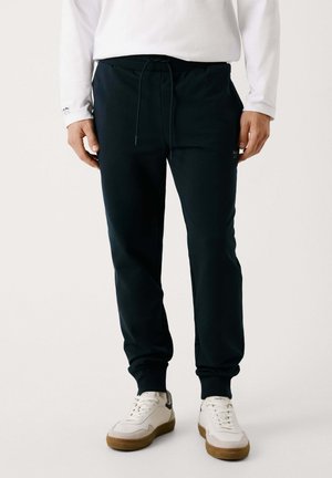 Mörkblå sweatpants med resårmidja, snörning och ribbade muddar. Bärs tillsammans med vita sneakers med en beige sula.