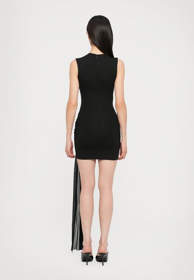 Abito mini senza maniche di colore nero con dettagli arricciati ai lati e una lunga frangia fluente. Tessuto liscio e silhouette aderente, abbinato a tacchi alti.