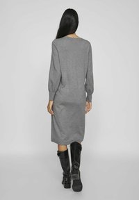 Vestito grigio a maniche lunghe realizzato in tessuto morbido, caratterizzato da una vestibilità ampia e un orlo fino al ginocchio. Indossato con stivali neri fino al ginocchio.