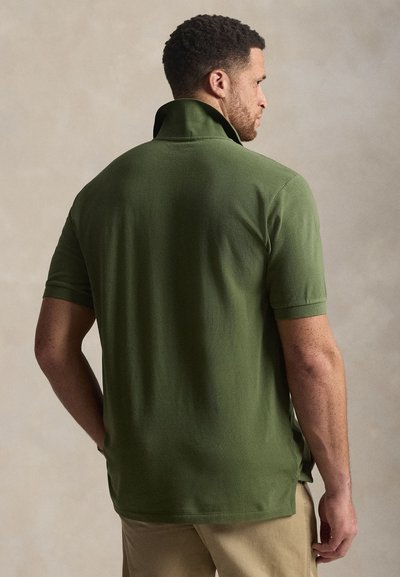 Πράσινο πόλο μπλουζάκι με γιακά, κοντά μανίκια και πλευρικές σχισμές. Δια θέτει λείος υφή και εφαρμοστή σχεδίαση, φαίνεται από πίσω.