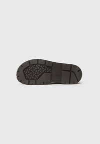 Semelle en caoutchouc noir avec un motif de semelle profond et des rainures. Présente une surface lisse et un talon renforcé. Construction durable pour une bonne adhérence.