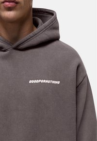 Grijze hoodie gemaakt van zachte stof, met een voorzijde logo geborduurd in lichtroze. Het ontwerp omvat een capuchon en geribde mouwen.
