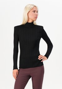 Long-sleeve black ribbed turtleneck top with a fitted silhouette and high neckline, paired with dark burgundy trousers.