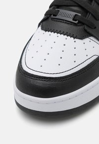 Shoe Puma com superior em couro preto, bico texturizado branco, ventilação perfurada e cadarços planos, apresentando uma placa de logotipo preta na lingueta.