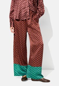 Spodnie o szerokich nogawkach w kolorze burgundowym w pomarańczowe kropki, z kontrastującym turkusowym wykończeniem. Gładki materiał i luźny krój.