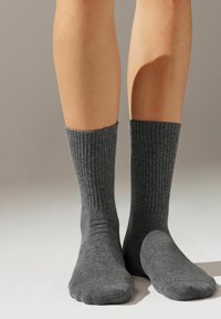 Calcetines grises acanalados, de longitud media hasta la pantorrilla, hechos de un material suave con una textura lisa y puntera reforzada. Diseño simple, sin patrones ni acentos.