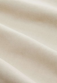 Beżowa tkanina o gładkiej, teksturowanej powierzchni i widocznym wzorze splotu, miękko opadająca z łagodnymi fałdami.