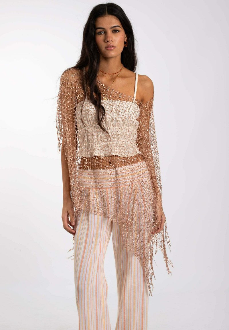 Top de ganchillo en beige con mangas de flecos, superpuesto sobre una camiseta blanca, combinado con pantalones de pierna ancha a rayas en tonos pastel. Tejido texturizado y transpirable.