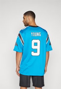 Carolina Panthers mez élénk türkiz színben, fekete és szürke részletekkel. A hátsó oldalon a "YOUNG" név és a "9" szám fehér színben, fekete kerettel látható.