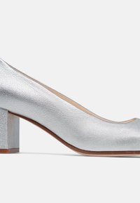 Pompe à talon bloc en cuir argenté avec un bout rond, une surface texturée et un accent en bois sur la semelle. Dotée d'une doublure intérieure lisse.