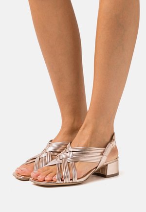 Sandales en métal rose doré à lanières avec un petit talon bloc et un design de dessus tissé, dotées d'une ouverture au niveau des orteils et d'une sangle de cheville réglable.