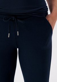Navy blue casual pants made of soft fabric, featuring an elastic waistband with a drawstring and metal tips, and side pocket.