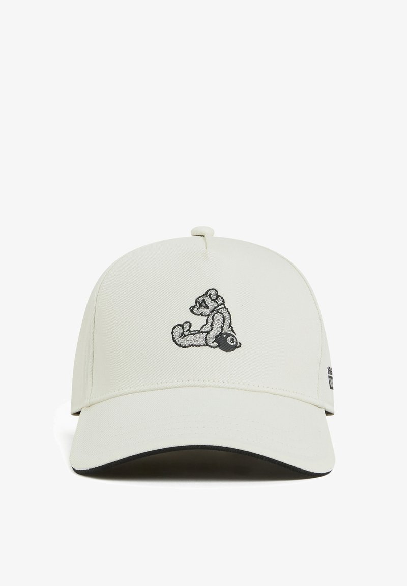 White cap with a curved brim, featuring a black embroidered bear graphic on the front and a small logo on the side. Textured fabric.