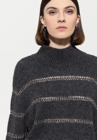 Grauer, gestrickter Pullover mit hohem Rippenkragen, der horizontale Streifen aus metallischem Garn aufweist. Weiche Textur und lockere Passform.