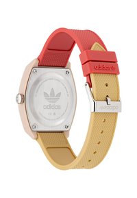 Adidas laikrodis su nerūdijančio plieno galiniu dangteliu, aštuonkampiu korpusu ir trijų spalvų silikono juosta: raudona, geltona ir smėlinė su tekstūruotais akcentais.