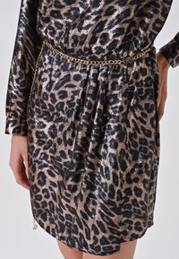 Abito leopardato nero e oro realizzato in tessuto lucido, con vita arricciata e una cintura in catena dorata, accompagnato da un delicato dettaglio plissettato.