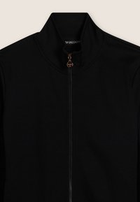 Giacca nera con zip e colletto alto, dotata di zip dorata e etichetta con logo. Tessuto morbido, leggero e design minimalista.