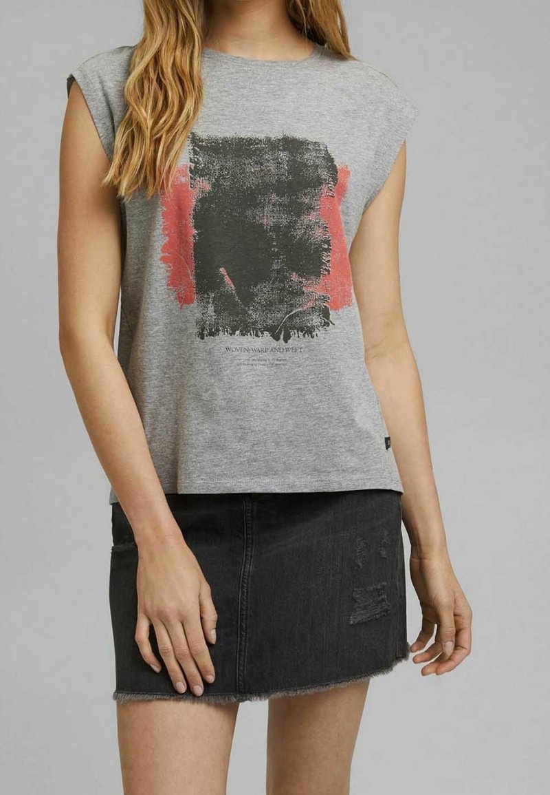 Grijze mouwloze t-shirt met zwart en koraalkleurig abstract patroon; gecombineerd met een zwarte denim rok met versleten accenten en een rafelige zoom.