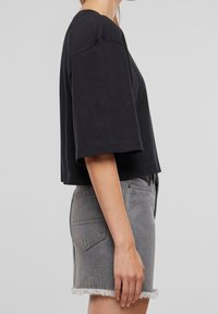 Černé zkrácené tričko s krátkými rukávy, z měkkého bavlněného materiálu; spárováno se šedou džínovou sukní s třásněmi na lemu a zadními kapsami.