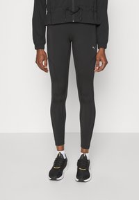 Zwarte sportleggingen met een gladde textuur, een aansluitend ontwerp en gestikte accenten. Gepaard met zwarte sneakers en een zwart jack.