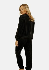 Ensemble de loungewear en velours noir comprenant un haut à coupe décontractée avec manches longues et un pantalon assorti. Le tissu a une texture douce et lisse.